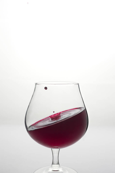 Wine glass with inclined level of wine and wine drop above it on - Valokuva, kuva