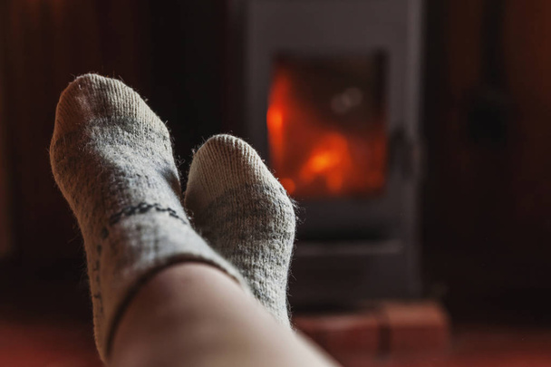 Pies piernas en ropa de invierno calcetines de lana en la chimenea en casa en invierno u otoño por la noche relajarse y calentar
 - Foto, Imagen