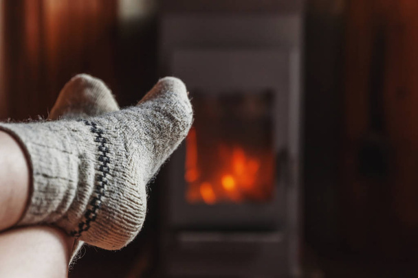 Feet legs in winter clothes wool socks at fireplace at home on winter or autumn evening relaxing and warming up - Photo, Image