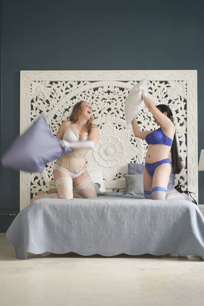 Además las mujeres de tamaño tienen pelea de almohadas en el dormitorio. gordito ladyes en lencería jugando
. - Foto, Imagen