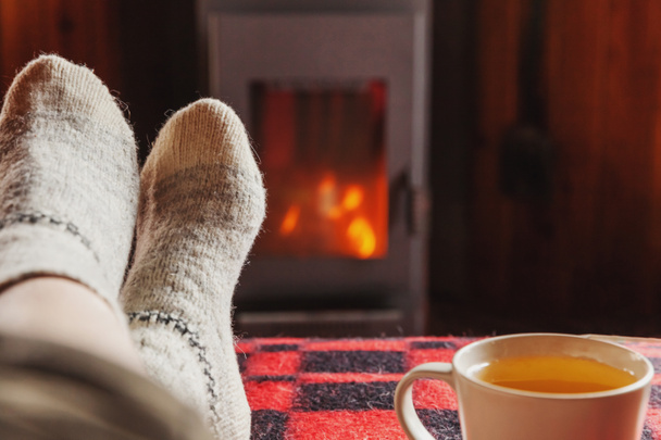 Nohy v zimních šatech s vlnohami a šálkem čaje u krbu doma v zimě nebo v podzimní noci relaxující a zahřívací - Fotografie, Obrázek
