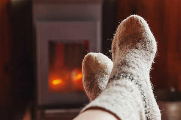 Feet legs in winter clothes wool socks at fireplace at home on winter or autumn evening relaxing and warming up - Фото, зображення