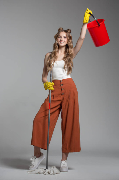 Mulher na moda com o cabelo longo mantém na mão um balde vermelho e uma esfregona
  - Foto, Imagem