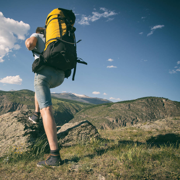Man walks along an asphalt road with a backpack on his back. Mountain background - Photo, Image