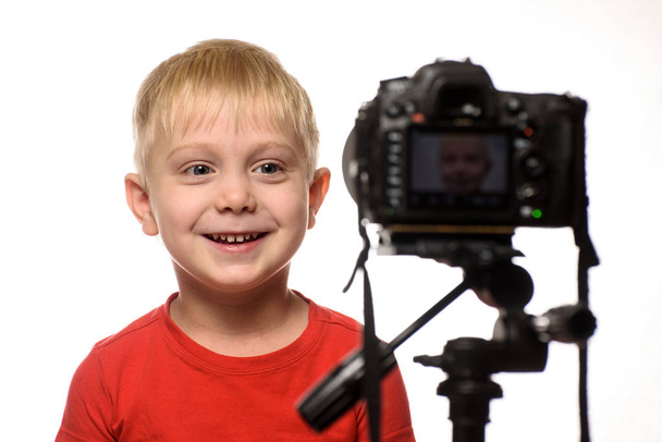 Garçon blond souriant devant l'objectif de la caméra. Petite blogueuse vidéo. Fond blanc
 - Photo, image