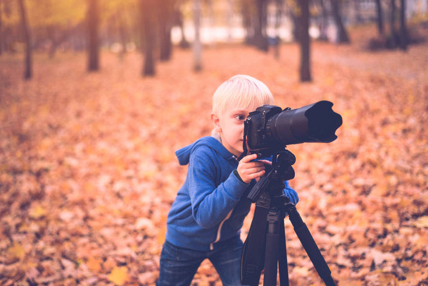 Kleine blonde jongen neemt Foto's op een SLR camera. Autumn Park - Foto, afbeelding
