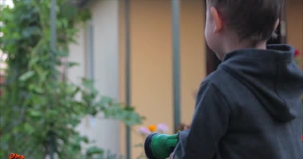V těsném záběru šťastného chlapce zalévání květin stříkací pistolí. Dítě se usmívá, představa dětských dobrodružství . - Záběry, video