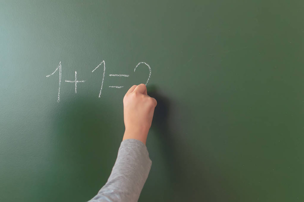 schoolboy hand writes in chalk on a blackboard during a lesson at school. - Zdjęcie, obraz