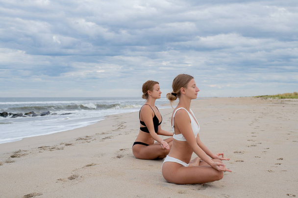 Νεαρές γυναίκες που εξασκούνται στη γιόγκα στη πόζα λωτού στην παραλία - Φωτογραφία, εικόνα