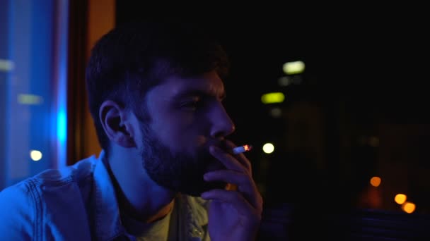 Young man smoking alone near window at night, worrying about life problems - Materiał filmowy, wideo