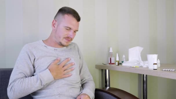 Sairas mies lääkitsee itseään kotona. Järkyttynyt nuori mies tarttuu rintaansa, koska keuhkoihin sattuu. Yöpöydällä on paljon lääkkeitä. Akuutti hengitystieinfektio. Kylmä flunssa. 4K
 - Materiaali, video