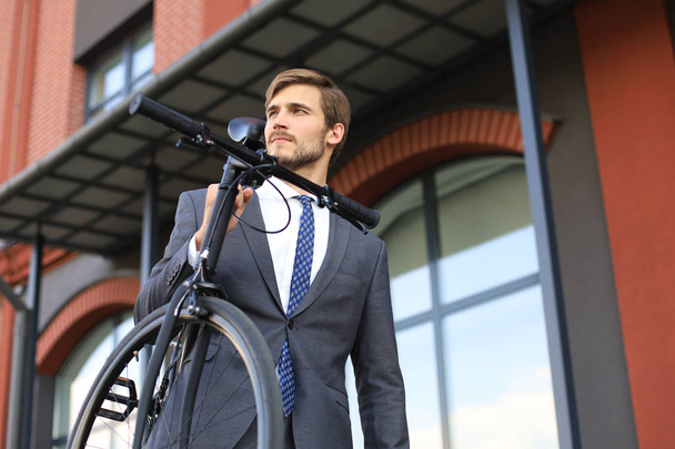 Handsome young businessman carrying his bicycle on shoulder while walking outdoors. - Fotografie, Obrázek