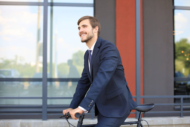 Young stylish business man dressed in suit riding on a bicycle on a city street. - Photo, image