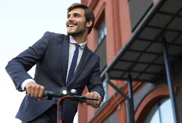 Young smiling business man in suit riding on electric scooter on a business meeting. Ecologic transport concept. - Valokuva, kuva