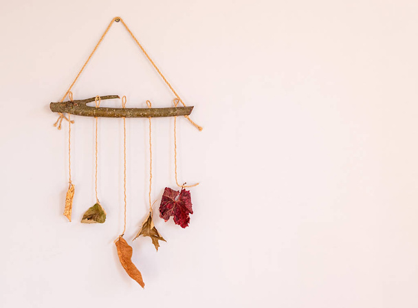 Осенняя композиция цветных листьев висит на деревянной палочке как элемент домашнего интерьера
 - Фото, изображение