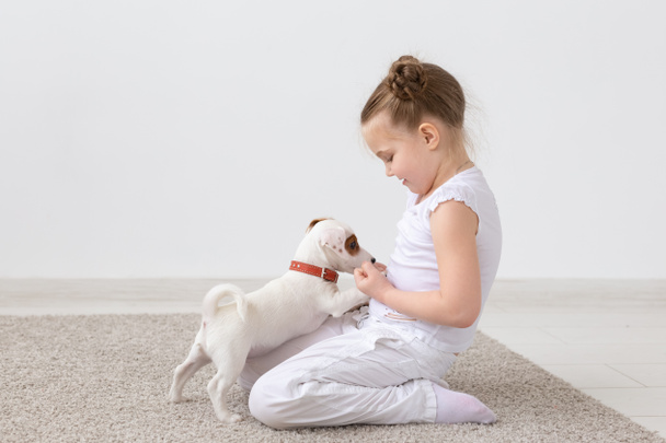 犬、ペットおよび子供のコンセプト - かわいい子犬が付いている床で遊ぶ子少女 - 写真・画像