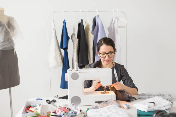 Mensen, kleermaker, naaister en fashion concept - lachende vrouwelijke modeontwerper met naaimachine - Foto, afbeelding