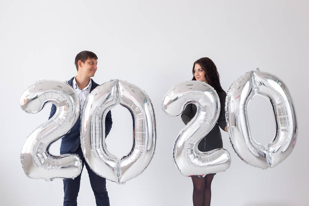 Yeni yıl, kutlama ve tatil konsepti - beyaz arka plan üzerinde yeni yıl için gümüş balonlardan yapılmış 2020 işareti ile eğlenen aşk çift - Fotoğraf, Görsel