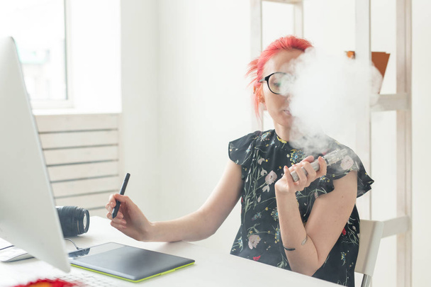 grafik tasarımcı kavramı - Kadın grafik tasarımcı ofiste masada grafik tablet kullanırken bilgisayar üzerinde çalışan ve bir vape sigara - Fotoğraf, Görsel