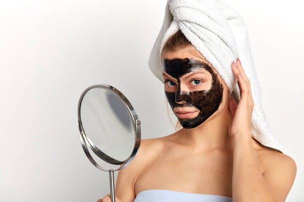 Young beautiful woman with a towel on her head has applied clay mask at home - Foto, imagen