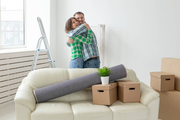 Young couple in denim pants embracing rejoicing in their new apartment during the move. The concept of housewarming and credit for new housing. - Фото, изображение
