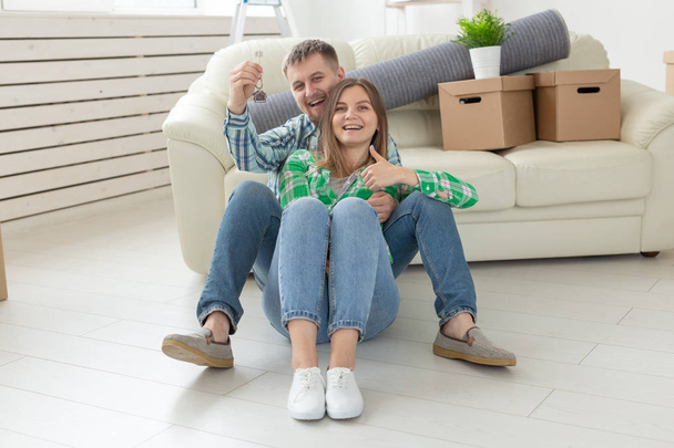 Charming young woman and her husband holding in hands the keys to their new apartment while sitting in her new living room. Housewarming and mortgage in new building concept - Foto, imagen