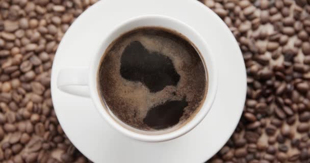Horní pohled na šálek horké kávy na tmavém pozadí plném kávových zrn. 4k výstřel - Záběry, video