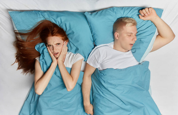 Unhappy woman closing her ears with palms and her snoring husband lying bedroom. - Foto, Bild