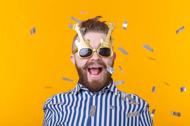 Сумасшедший радостный веселый молодой человек в кепке и очках на желтом фоне. Концепция успешной вечеринки и праздника
. - Фото, изображение