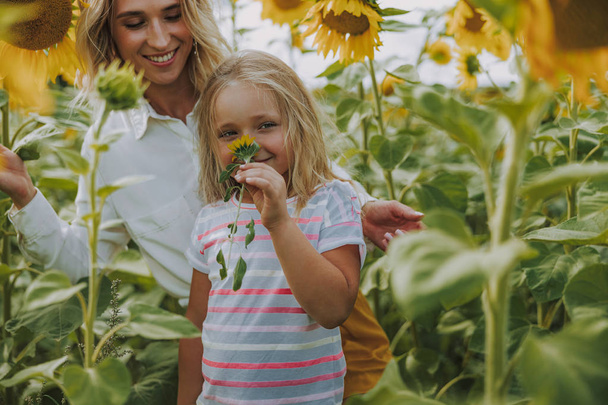 Blonde lady and cute girl standing in the field of sunflowers - Φωτογραφία, εικόνα