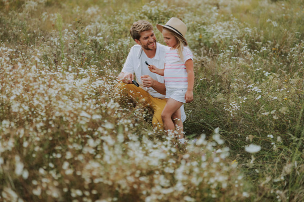 Smiling dad with pretty little daughter using loupe in field - Фото, зображення