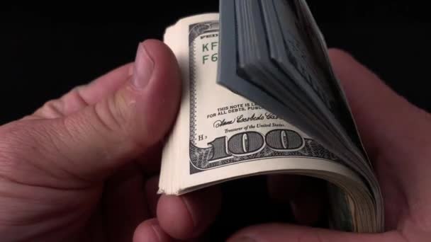 Mies laskee dollareita mustalla pohjalla. Miehen käsissä on nippu amerikkalaista rahaa. Tarkistan satasen seteleitä väärennöksen varalta. Käsite: rikkaus, rikastuminen, väärennetyn rahan todentaminen
. - Materiaali, video