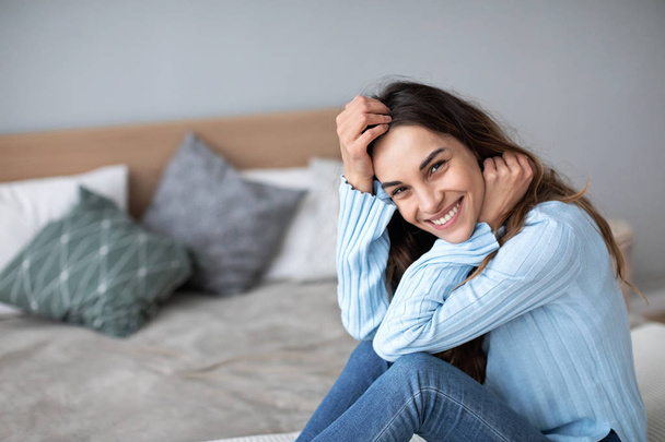 Gorgeous young smiling woman is sitting on the couch and looks on camera. - Fotoğraf, Görsel
