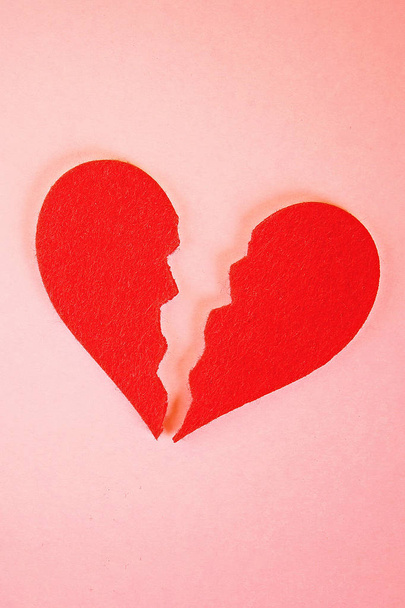 Corazón de fieltro rojo roto en dos mitades sobre fondo rosa
. - Foto, Imagen