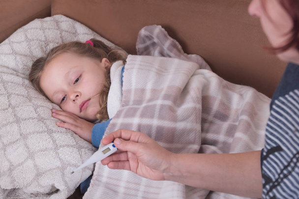 Sick little girl in bed. Mother with thermometer is sitting near the bed. - Foto, afbeelding