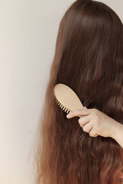 girl with long brown hair combing them with a wooden comb, vertical, close-up - Фото, зображення