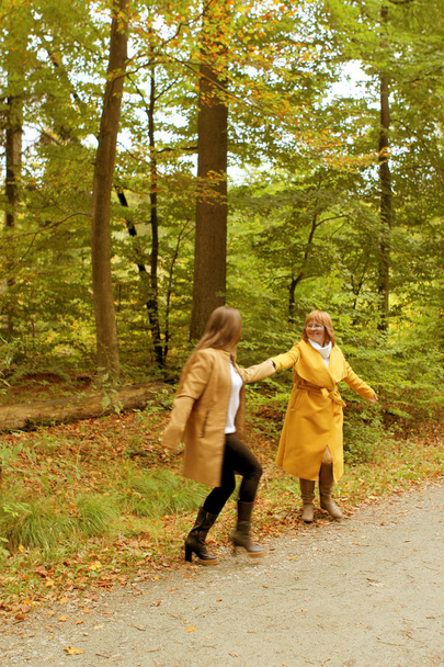 two people, mother and daughter, a woman and a young girl holding hands, dancing in a yellow autumn park, concept of family relationships, generation - Foto, Imagem