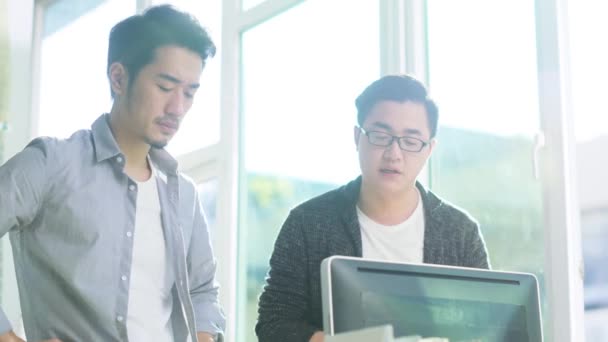 dva mladí asijští podnikatelé, kteří stojí na stole a analyzují data pomocí stolního počítače - Záběry, video