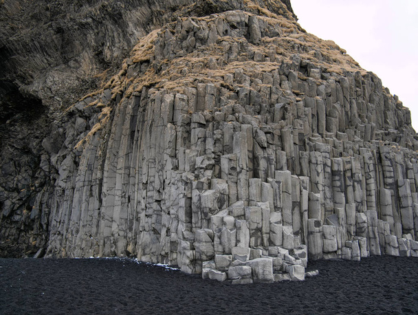 Rotswand met basalt steentjes en zwart zand - Foto, afbeelding