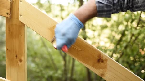 Ενήλικος τεχνίτης ξυλουργός με το πινέλο ζωγραφίζει τα συμβούλια ενός ξύλινου φράχτη. Στο νοικοκυριό, κάντο μόνος σου. Πλάνα. - Πλάνα, βίντεο