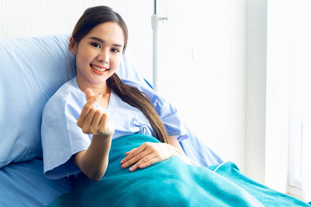 Aziatische jonge vrouwelijke patiënten tonen een mini-hart symbool met een glimlach - Foto, afbeelding