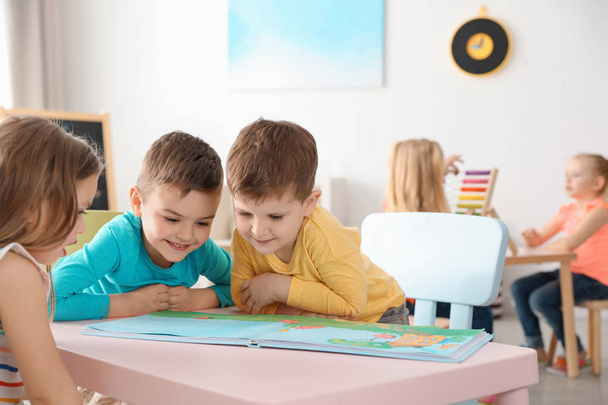 かわいい小さな子供たちは、屋内のテーブルで本を読んで。学習と遊び - 写真・画像