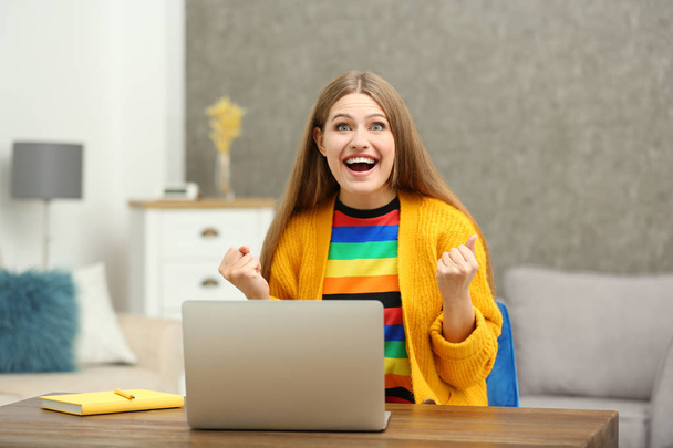 Ευτυχής νεαρή γυναίκα παίζοντας online λοταρία χρησιμοποιώντας το laptop στο σπίτι - Φωτογραφία, εικόνα