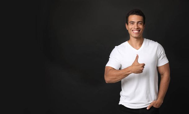 Handsome young African-American man showing thumbs-up gesture on black background - Foto, Imagen