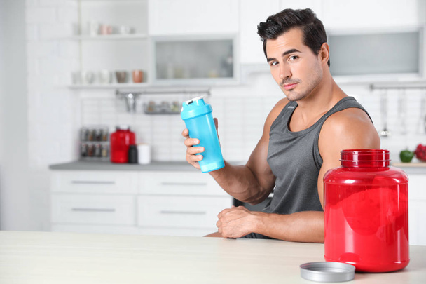 Young athletic man with protein shake powder in kitchen, space for text - Фото, зображення