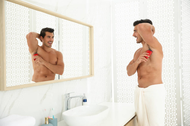 Handsome young man applying deodorant in bathroom - Photo, Image