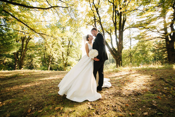 junge Braut mit Bräutigam beim Spaziergang im Wald. Frau mit langem weißen Kleid und Mann im schwarzen Anzug mit Krawatte - Foto, Bild