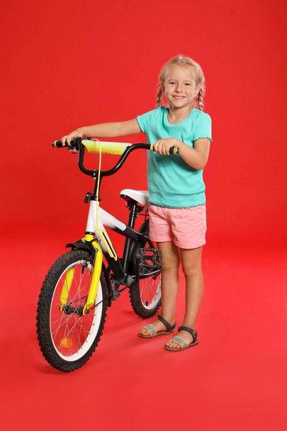 niedliches kleines Mädchen mit Fahrrad auf rotem Hintergrund - Foto, Bild