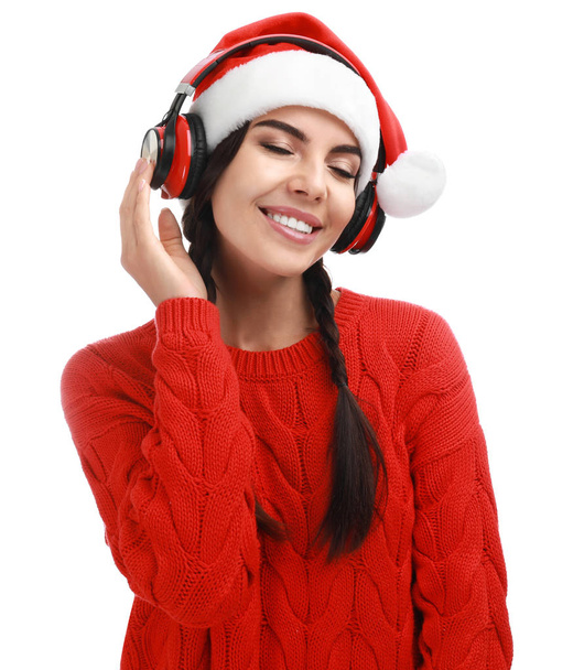 Young woman in Santa hat listening to Christmas music on white background - Photo, image