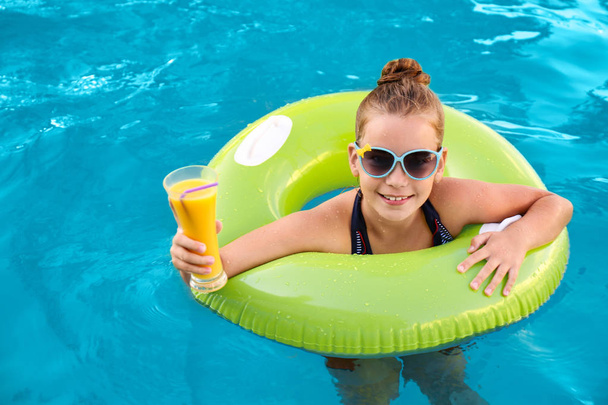 Happy little girl with inflatable ring and drink in swimming pool - Fotoğraf, Görsel